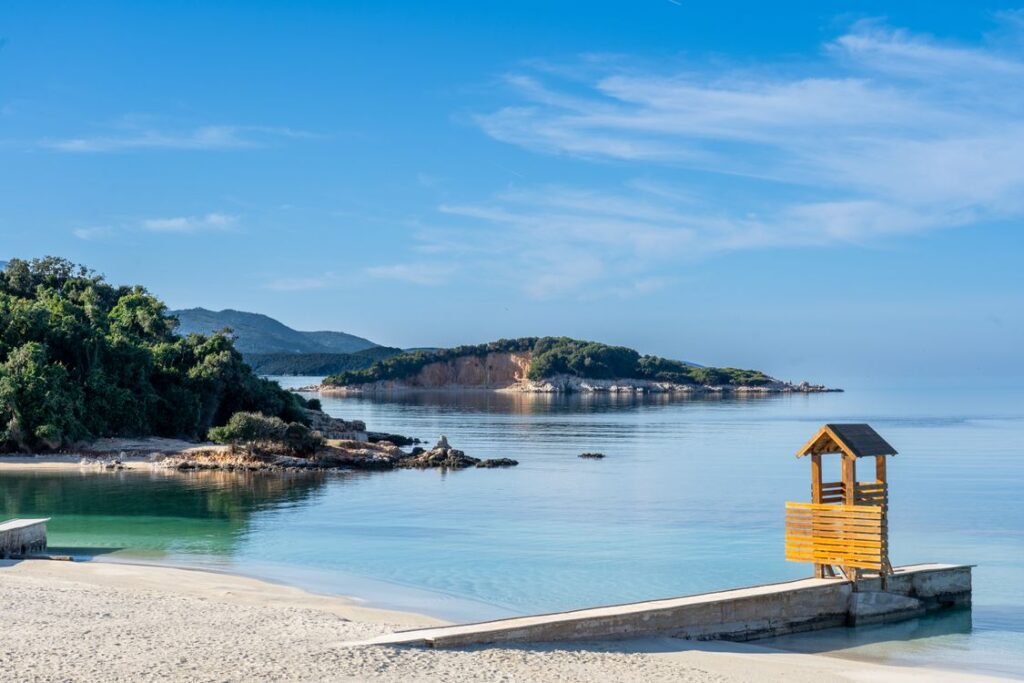 Turquoise water, sandy Ksamil beach and a green island with mountains behind, one of the places to visit before they get expensive